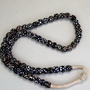 Black Antique Skunk Trade Beads come on a strand. They have a white dot, and some have another colored dot on them in green, blue, red, and pink.