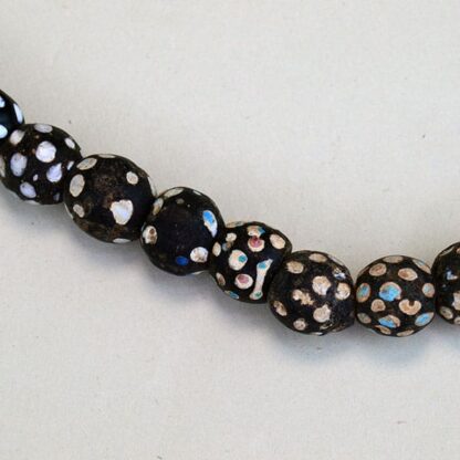 Black Antique Skunk Trade Beads come on a strand. They have a white dot, and some have another colored dot on them in green, blue, red, and pink.