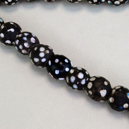 Black Antique Skunk Trade Beads come on a strand. They have a white dot, and some have another colored dot on them in green, blue, red, and pink.