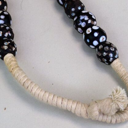 Black Antique Skunk Trade Beads come on a strand. They have a white dot, and some have another colored dot on them in green, blue, red, and pink.