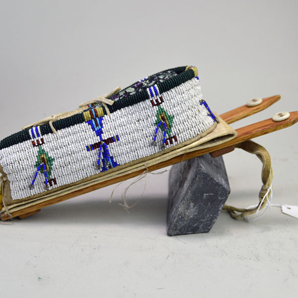 This Cheyenne-style toy cradle features wood base and a rawhide platform, fully beaded with 13/0 cut seed beads and secured with sinew stitching—showcasing traditional craftsmanship in miniature form.