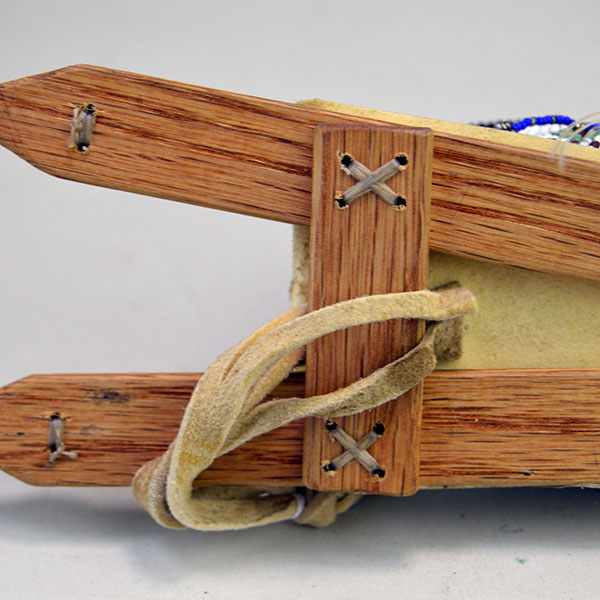 Pictured here are the wood base from a Cheyenne-style toy cradle, crafted with a rawhide platform and fully adorned in 13/0 cut seed beads, each detail secured with sinew stitching to reflect traditional artistry in miniature form.