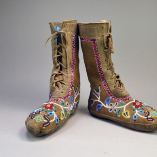 These Cree-style high-top moccasins are handcrafted from smoked moosehide leather, featuring soft soles and adorned with vibrant floral beadwork , and quill work that reflects traditional woodland design