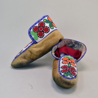 These Cree-style moccasins, crafted from smoked brain-tanned moosehide leather, feature vibrant floral beadwork that adorns both the vamp and the cuffs, celebrating Woodland tradition with every stitch.