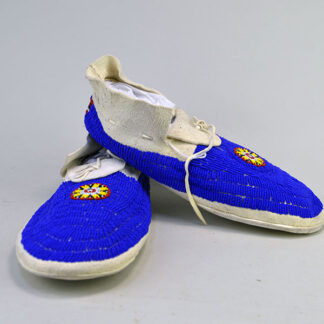These striking blue beaded moccasins are crafted from soft white deerskin and sewn with thread. Fully adorned in lazy stitch beadwork. One of a Kind.