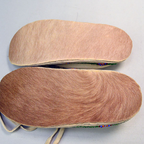Pictured here are the rawhide soles with natural hair on these Northern Plains-style child’s beaded moccasins, highlighting the traditional materials and enduring craftsmanship beneath the vibrant design.