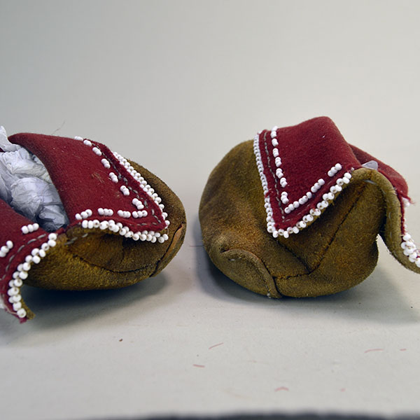 Pictured here is the back of a pair of Eastern Woodland-style moccasins, hand-sewn with sinew and fully lined in red wool, showing areas of bead loss where some decorative elements have fallen away.
