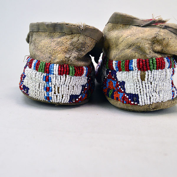 In this picture of the Antique Moccasins—Northern Plains Style, the back reveals damage to the trim fabric, indicating signs of age and wear.