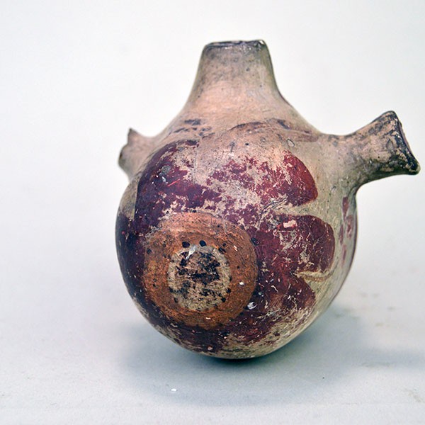 Close up view of small canteen Acoma style decorated with floral design on one side and red on the other.