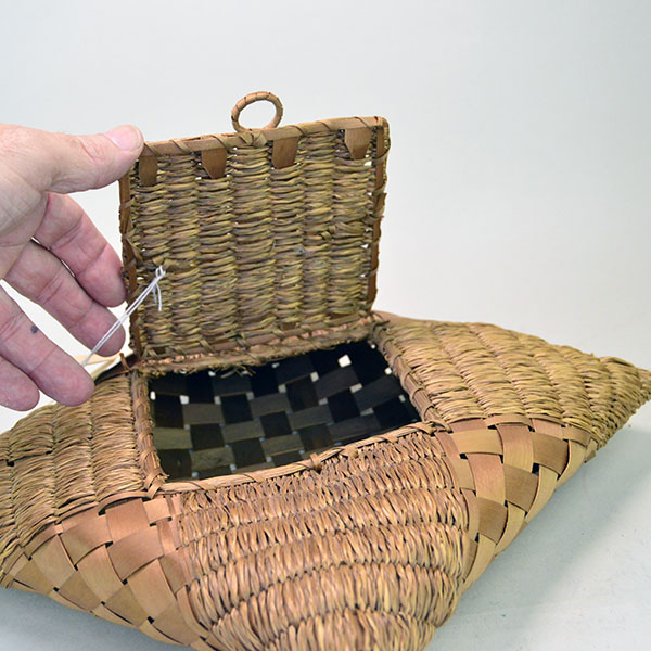 Pictured here is a Passamaquoddy handkerchief basket featuring a finely crafted handled lid, skillfully woven from sweetgrass and ash.
