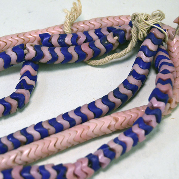 Pictured here are antique trade beads—snake beads in mixed rose and cobalt blue tones—interlocking in a vibrant, serpentine strand.