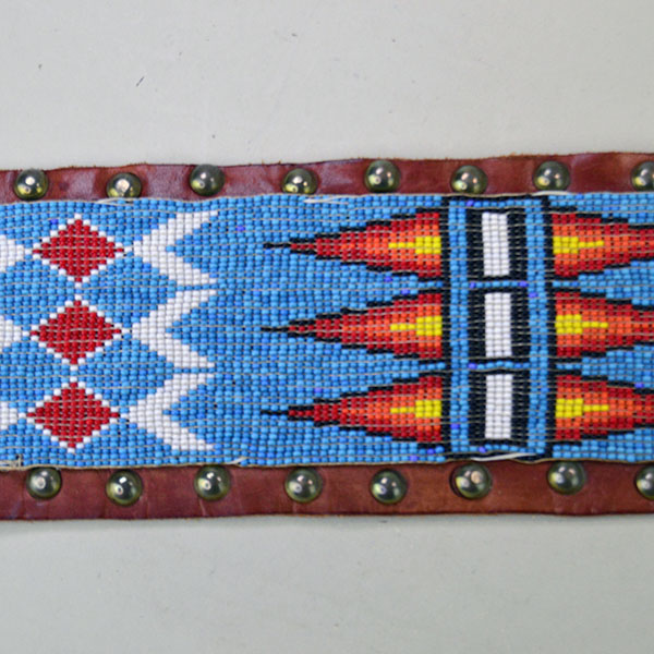 This vintage handcrafted belt, beaded in blue with a geometric design, is pictured here showcasing its intricate beadwork along with the .25-inch brass tacks and .5-inch brass spots