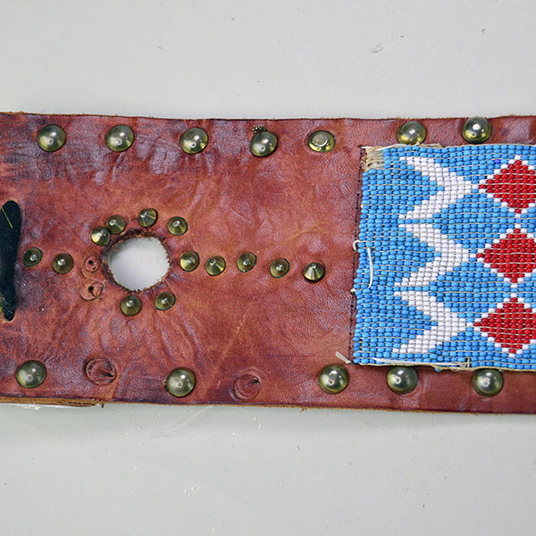 This vintage handcrafted belt, beaded in blue with a geometric design, is pictured here showcasing its intricate beadwork along with the .25-inch brass tacks and .5-inch brass spots