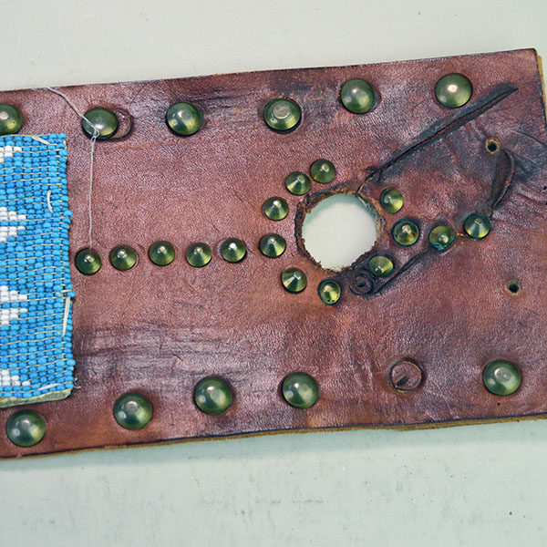 This vintage handcrafted belt, beaded in blue with a geometric design, is pictured here showcasing its intricate beadwork along with the .25-inch brass tacks and .5-inch brass spots