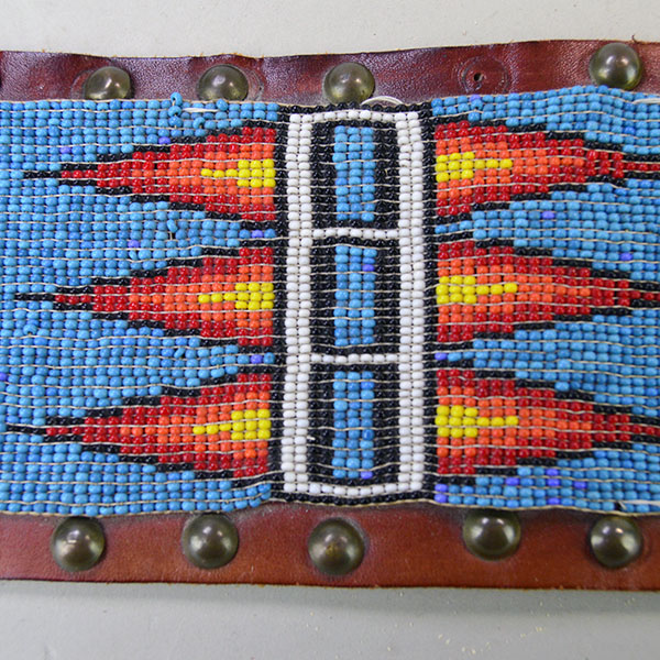 This vintage handcrafted belt, beaded in blue with a geometric design, is pictured here showcasing its intricate beadwork along with the .25-inch brass tacks and .5-inch brass spots