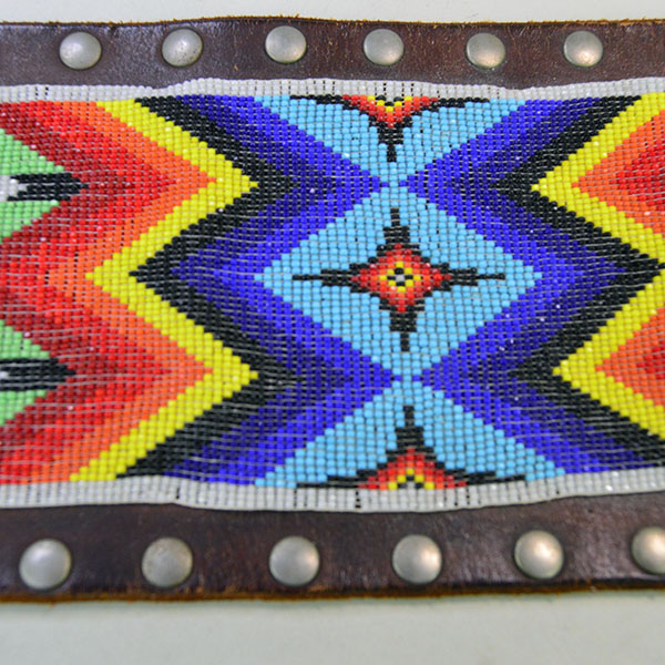 This belt features a beaded feather design crafted with 13/0 cut seed beads and accented by silver rivets
