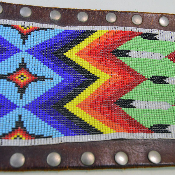 This belt features a beaded feather design crafted with 13/0 cut seed beads and accented by silver rivets