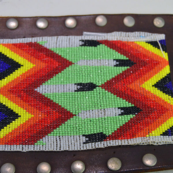 This belt features a beaded feather design crafted with 13/0 cut seed beads and accented by silver rivets