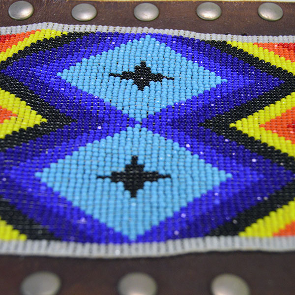 This belt features a beaded feather design crafted with 13/0 cut seed beads and accented by silver rivets