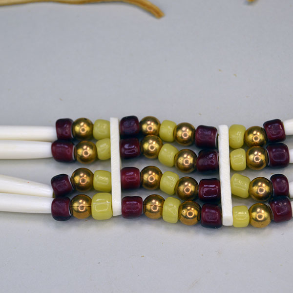 four row No Drop Choker comes with 1.5 inch Bone Hairpipe . This Choker measures 16 inches long with 10‑inch ties. One of a Kind. Pictured here is the white center cranberry, greasy yellow crow beads, brass beads and the bone spacers.