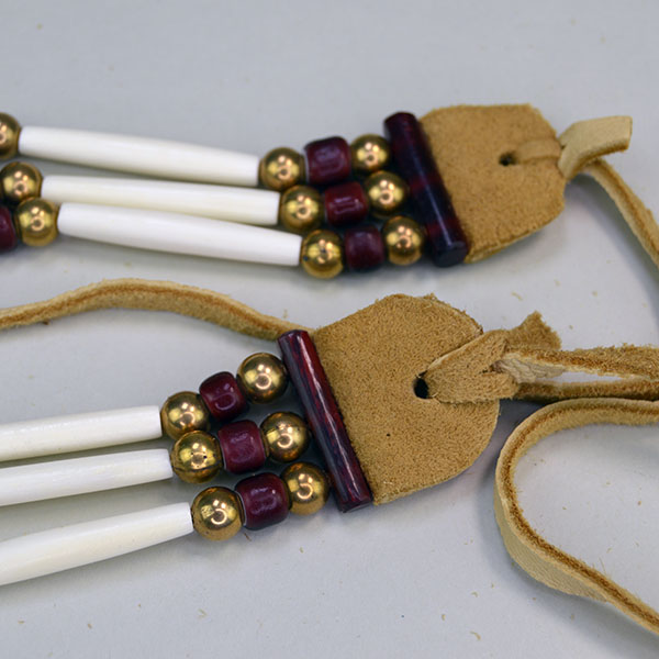 three‑row Choker- White Center Cranberry stands out with its striking mix of bone, brass, and deep cranberry‑colored crow beads. measures 16 inches long. the picture is of the end of the choker with he beads, the spacer and the deerskin lacing.