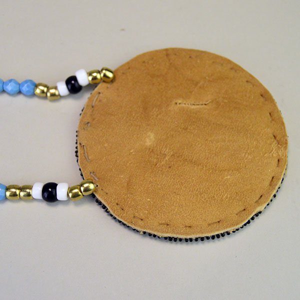 Necklace- Rosette Beaded Thunder Bird and Tipi. 13/0 Cut Seed Beads. Rosette measures approximately 4″ in diameter. One of a Kind. pictured here is showing the Braintan Leather Backing.