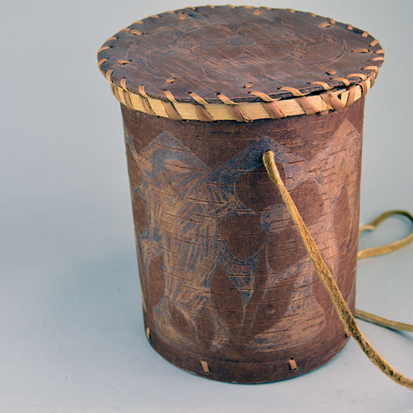 Floral‑Etched Birchbark Basket with Lid Container features Floral etchings around the container and the cover. approx. 9" tall x 8" in diameter. One side showing the etching and the leather strap.