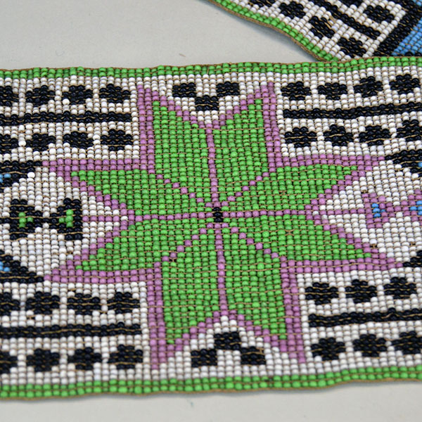 Sash- Antique Loom Beaded showcases a bold floral design. Approx. 24" partially braided wool‑yarn fringe. the sash reaches approx. 55" in total length. A green beaded floor with a rose color outline.