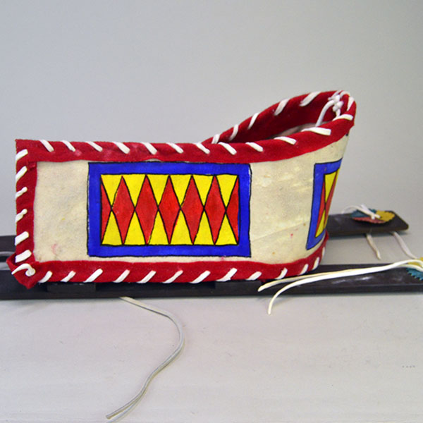 Cradleboard Parfleche features rawhide construction and a hand‑painted design. measures approximately 21 inches long, 7 inches wide at the head. The side of the cradleboard.