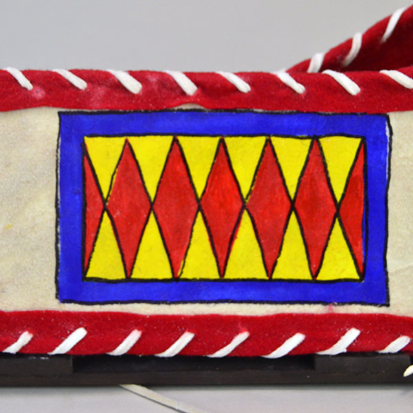 Cradleboard Parfleche features rawhide construction and a hand‑painted design. measures approximately 21 inches long, 7 inches wide at the head. The design on the side with the red wool around the edges.