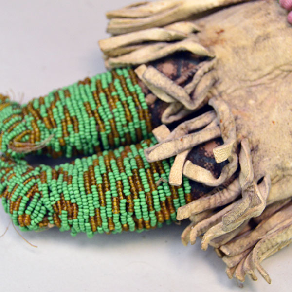 This antique Doll- Northern Plains Style offers exceptional handmade detail and strong visual presence. She stands approx. 14 inches tall. One of a Kind. The beaded moccasins against the Braintanned dress.