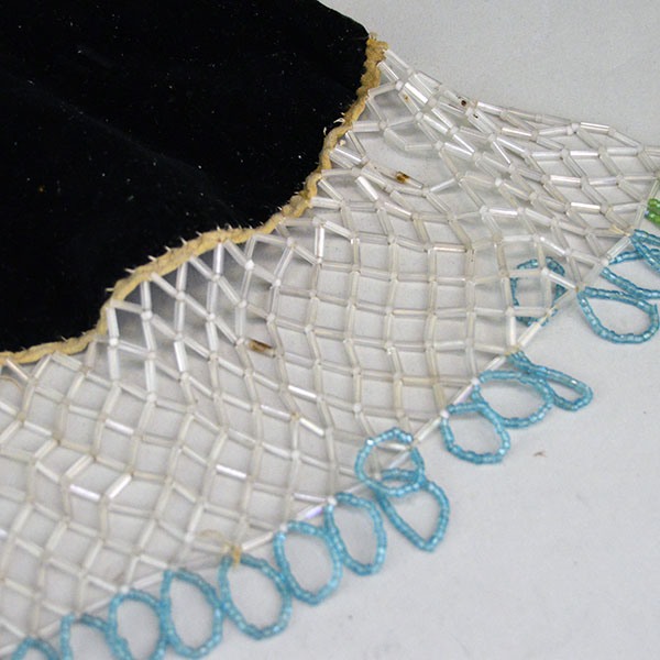 This floral beaded cape dates from the 1950s to 1960s and features an elaborate net fringe. few beads are missing, consistent with age and use. The bead net around the cape.