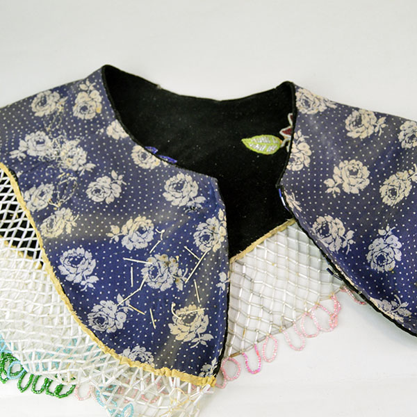 This floral beaded cape dates from the 1950s to 1960s and features an elaborate net fringe. few beads are missing, consistent with age and use. The floral calico blue lining.