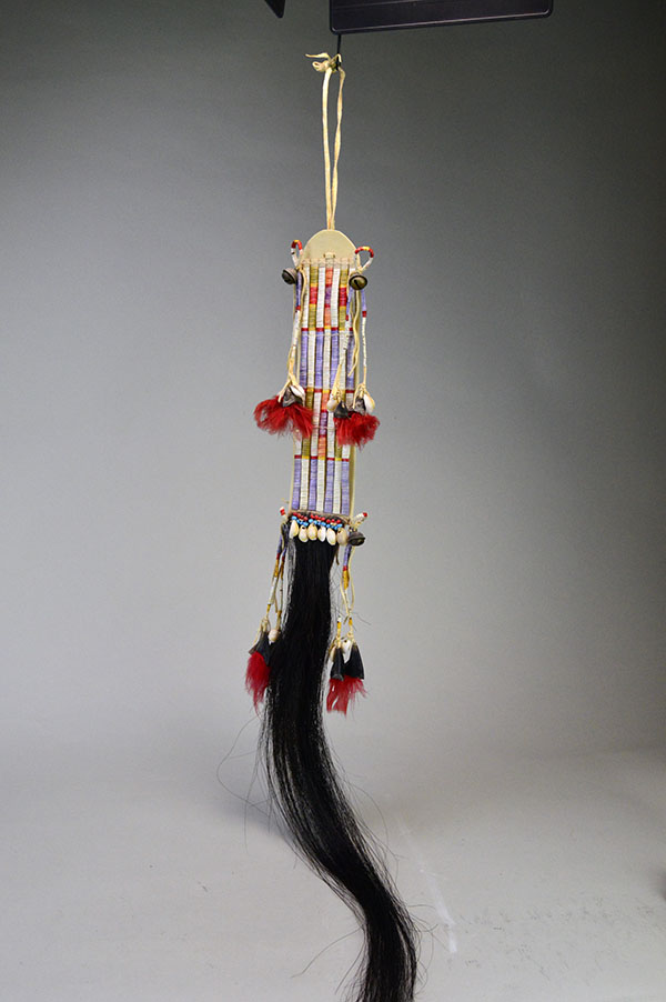 Wapegnaki- Hair Ornament Quilled features 9″ of quillwork on a 10″ rawhide base. Eight 5″ quilled tassels hang from the piece, 23″ dark horse‑hair drop.