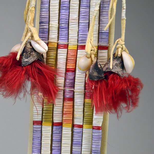 Wapegnaki- Hair Ornament Quilled features 9″ of quillwork on a 10″ rawhide base. Eight 5″ quilled tassels hang from the piece, 23″ dark horse‑hair drop. The middle showing the quill work, the bells, the cowrie shells.