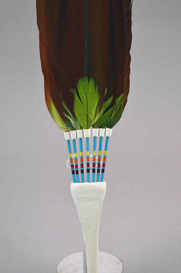 Flat Fan- With Macaw Feathers, vivid green accents, white leather handle with tassels, and bold color for regalia or display. Measures 18.5 inches long. Pictured here is the vibrant green feathers against the red feathers with the colorful thread wrapped base.