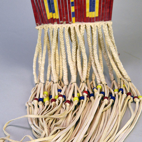 Pipe Bag- Double-sided Quillwork, Braintanned deerskin, braided fringe, cone‑drop tassels, and brass bells. Measures 45" with light age wear. The fringe on the bottom of the bag