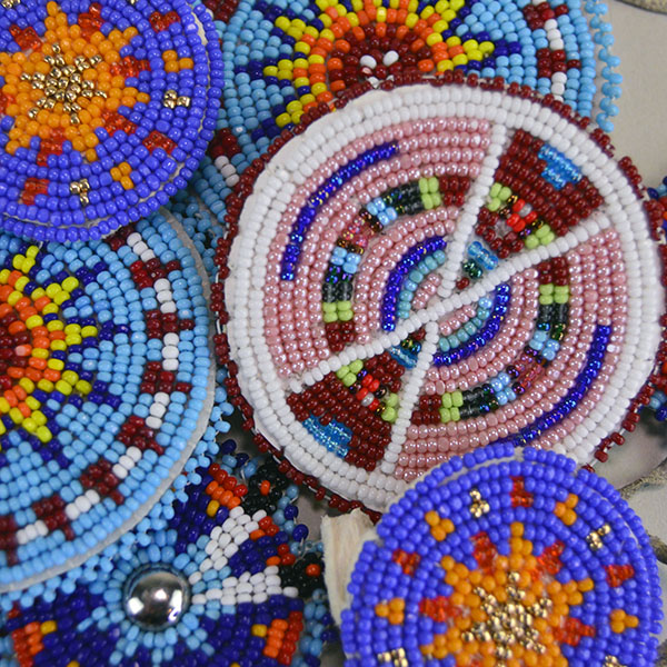 Seven‑piece Rosette Group Lot featuring matching sets, a pin rosette, Braintanned lacing, and dimensional edging. The lot offers mix of sizes. one of a kind. A close up of the beautiful colors in the rosettes.