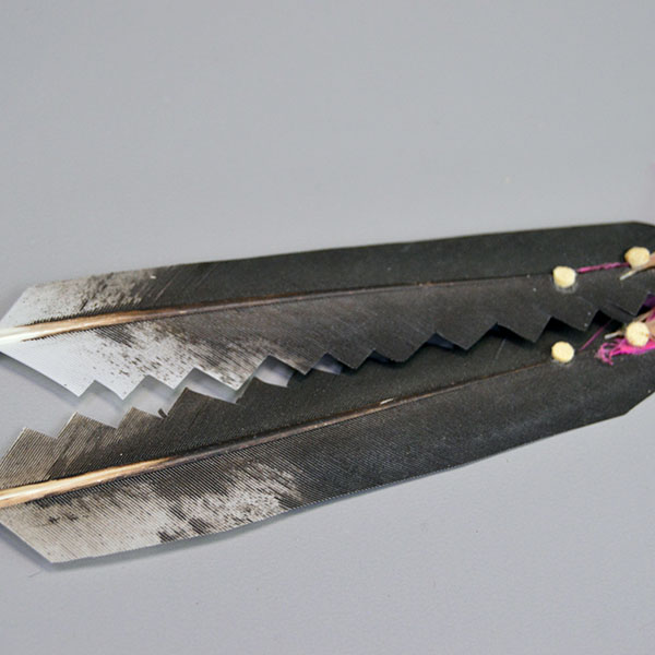 Scalp Feather- Stamped Concho, Hand‑painted scalp feather with a stamped concho, cut designs, pink fluffs, and traditional detailing. Measures 12.5 inches. Pictured here is the cut design on the feathers and the tiny white leather dots.