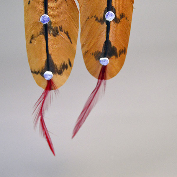Hand‑painted turkey scalp feathers with a vibrant 11/0 beaded rosette, red accent tip, and deerskin wrapping for a balanced, traditional regalia finish. Pictured here is the tine blue dots on the front of the feathers and the red accent feathers on the tips.