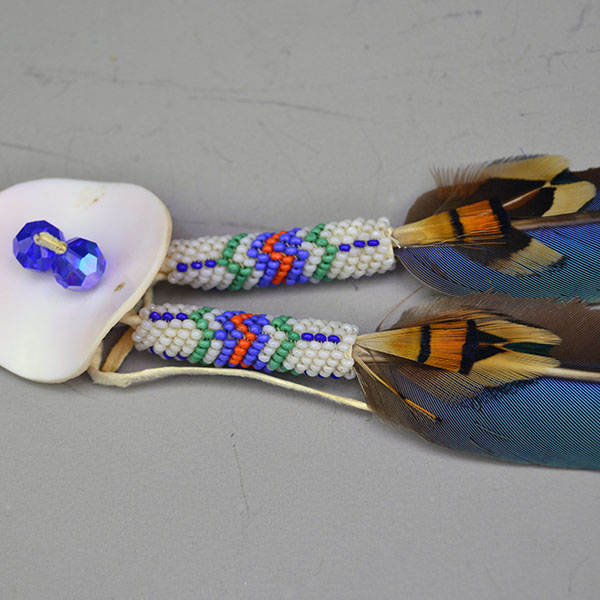 This striking Blue Macaw Scalp Feather & Conch blends bold natural feathers with detailed beadwork and traditional beadwork. Pictured here is the pink concho and the peyote stich at the bottom of the feathers with the accent feathers.