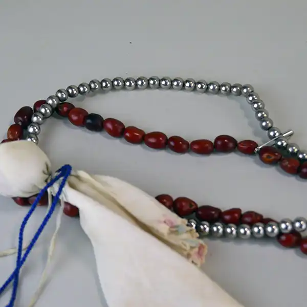 Bandolier- Nickel & Mescal Beads with a pink shell centerpiece, blue fire‑polished bead, and a 5‑inch drop. and in good usable condition. Approx. 36" long . Showing the red mescal beads and the nickel beads.