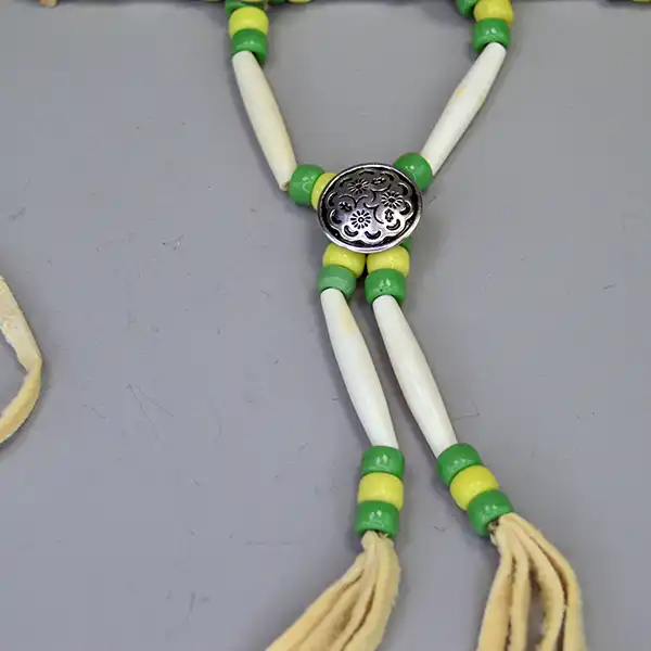 Handcrafted bone hairpipe Choker- Green & Yellow Crow beads, white-center pony beads, deerskin leather. approx. 15 inches. One of a Kind. Pictured here is the decorative button on the drop.