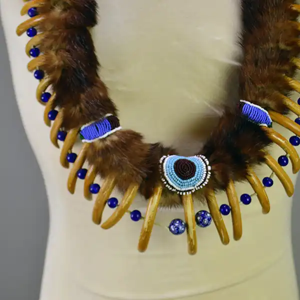 Necklace- Carved Bear Claw with cobalt blue glass beads and a removable ribbon work drop featuring beadwork, silver brooches, and otter fur. One of a Kind. The necklace with the beaded accents , the bear claws, and the beads.