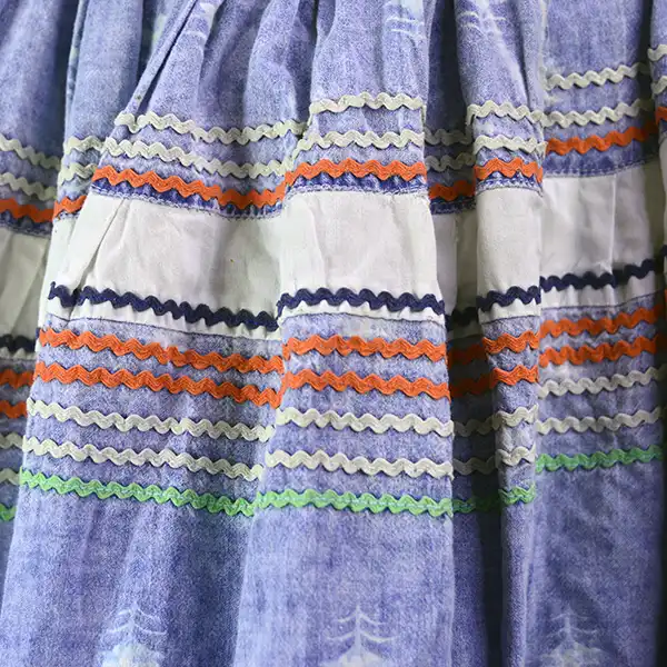 Vintage calico Seminole‑style patchwork skirt with multicolor rickrack, vibrant piecework, and traditional craftsmanship; shows gentle wear. One of a kind. Pictured here is the ric-rac design in navy blue,, orange light green and white.