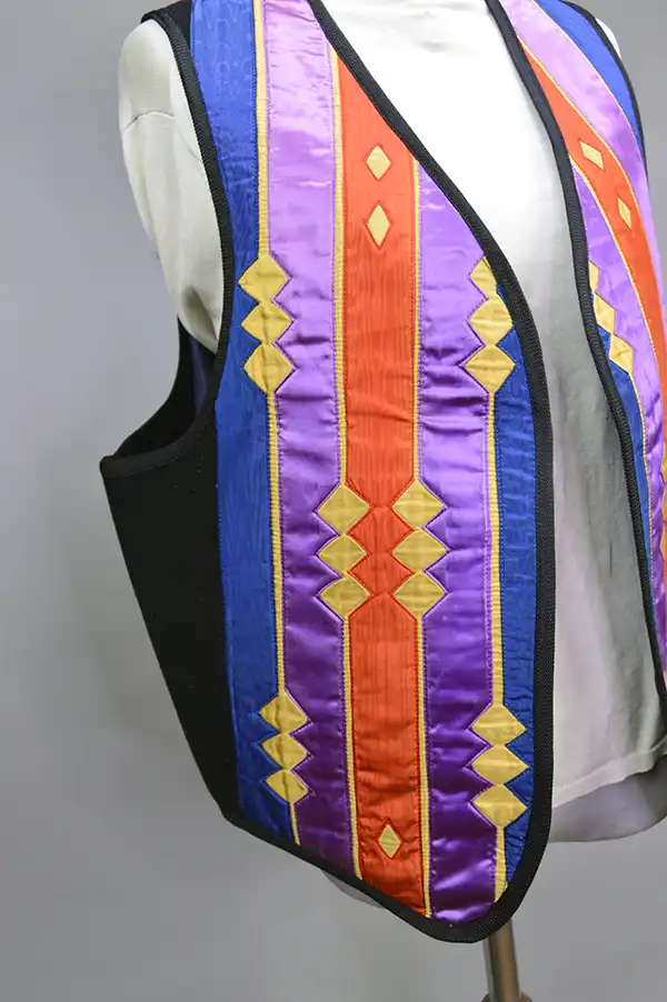 Contemporary Vest- Ribbon Work featuring vibrant purple, orange, gold, and blue designs, black fox braid trim, silk lining, and a red corduroy back. the ribbon work design.